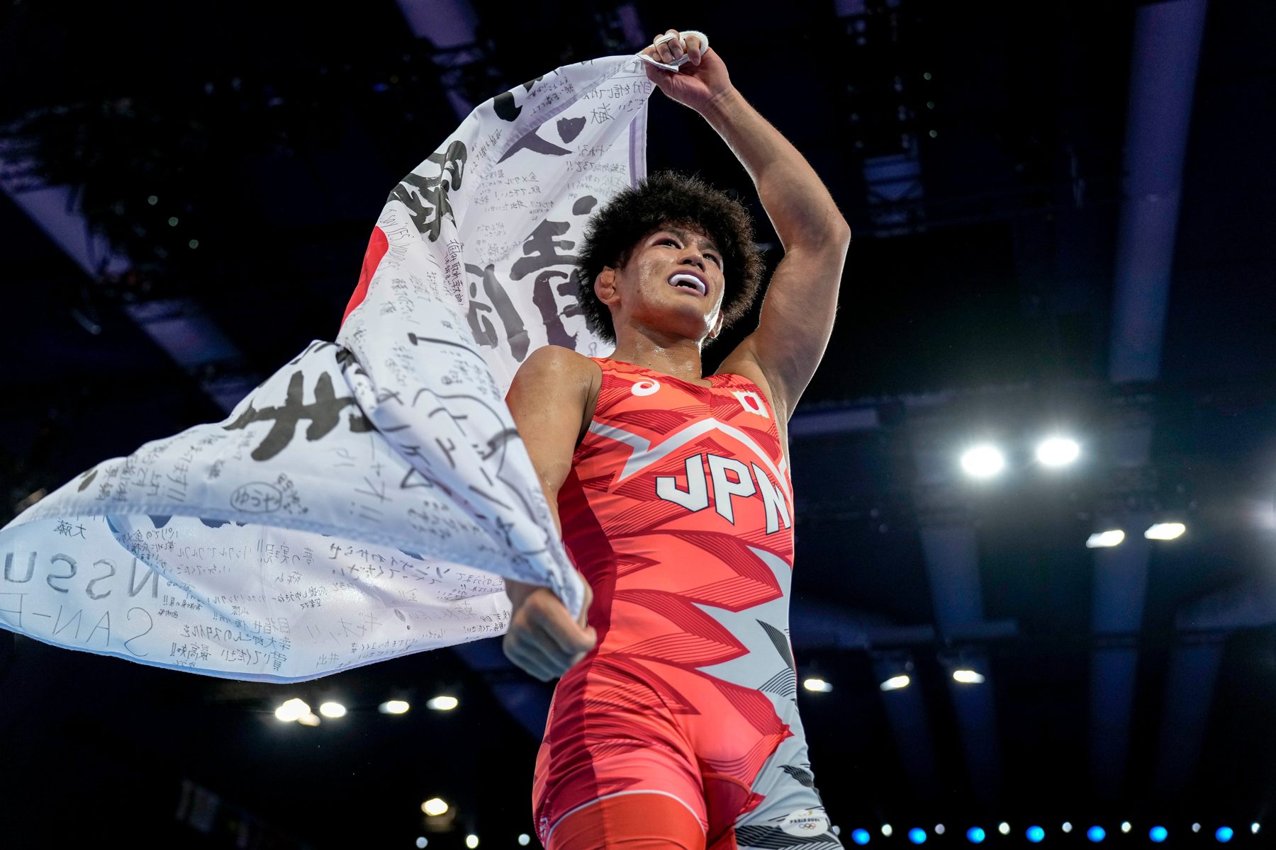 Kotaro Kiyooka raising a Japanese flag covered in handwritten messages after his Paris final