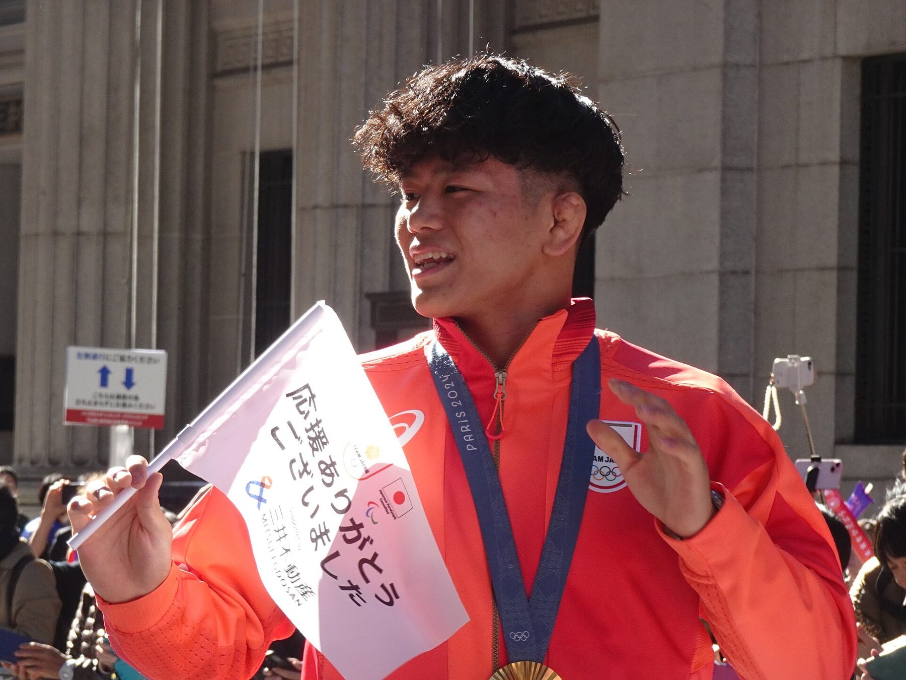 Kotaro Kiyooka waving a small thank-you flag to the crowd during the Team Japan parade in Nihonbashi